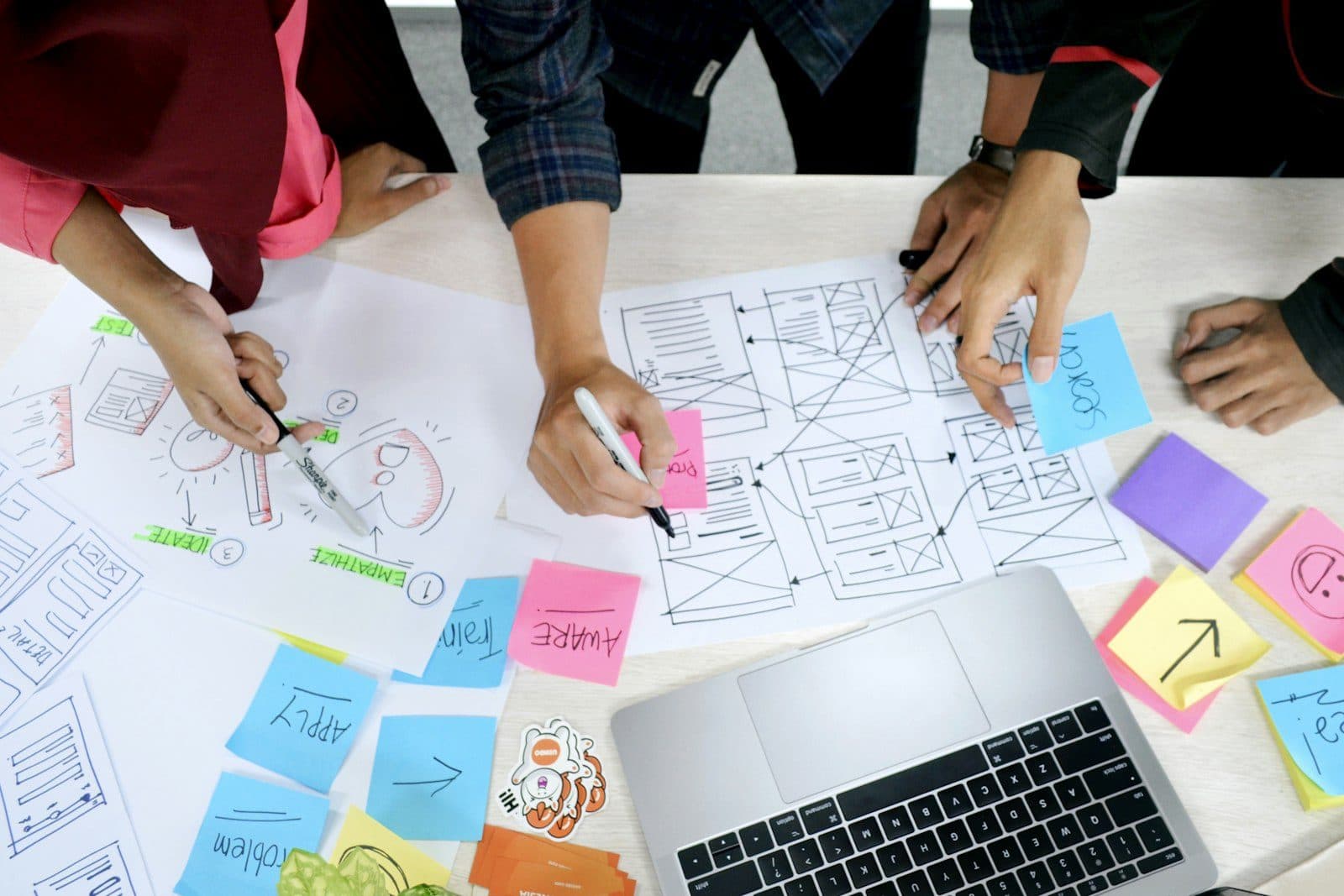 Designers sketching wireframes on paper next to a laptop